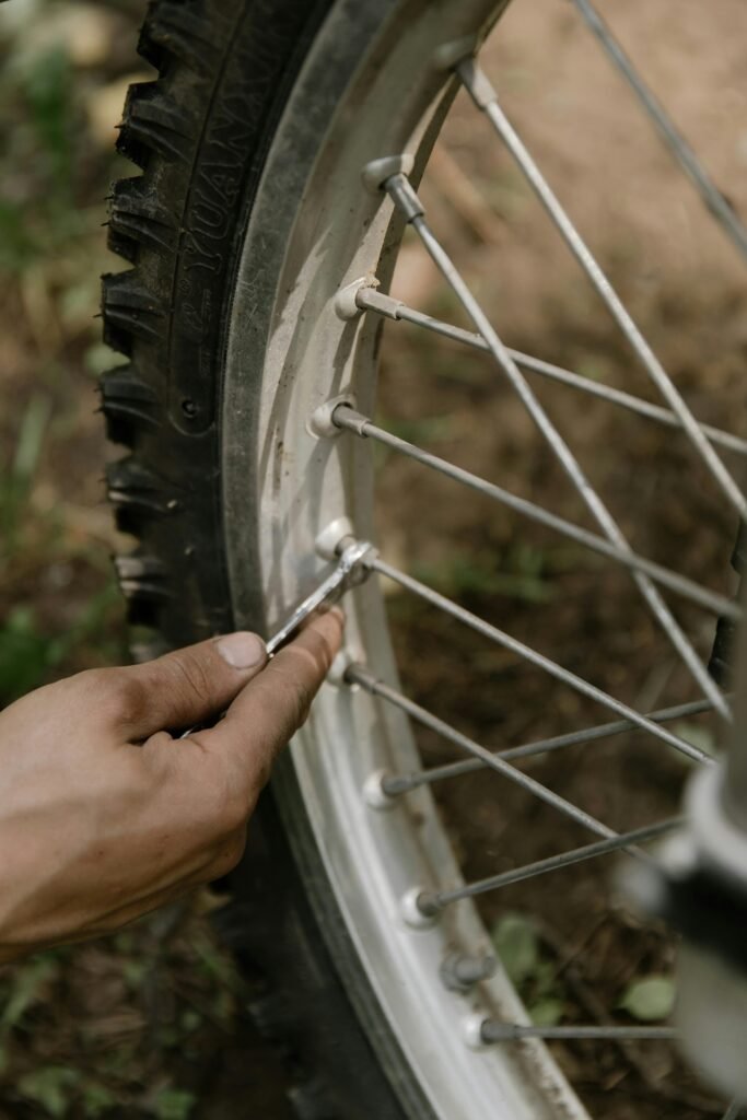 Close-up of a mechanic's hand tightening the spokes of a motorbike tire outdoors.